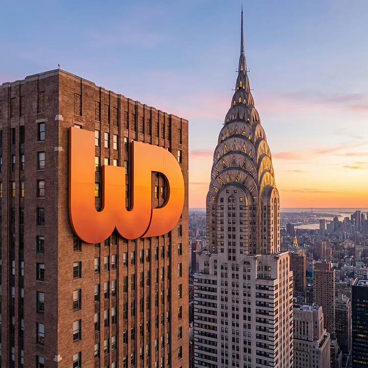 New York City skyscraper at sunset featuring a large orange Womp Designs logo next to the Chrysler Building.