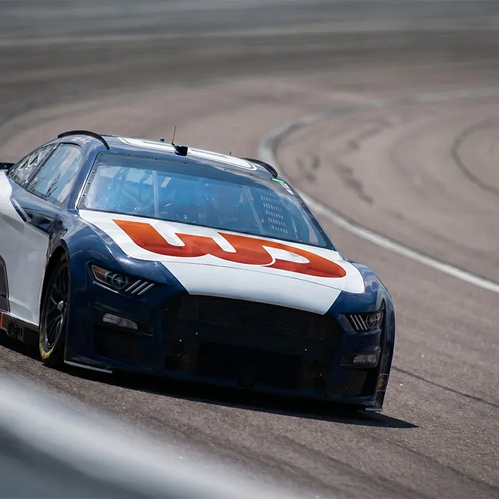 Race car speeding around a track with a red and orange Womp Designs logo on the hood.