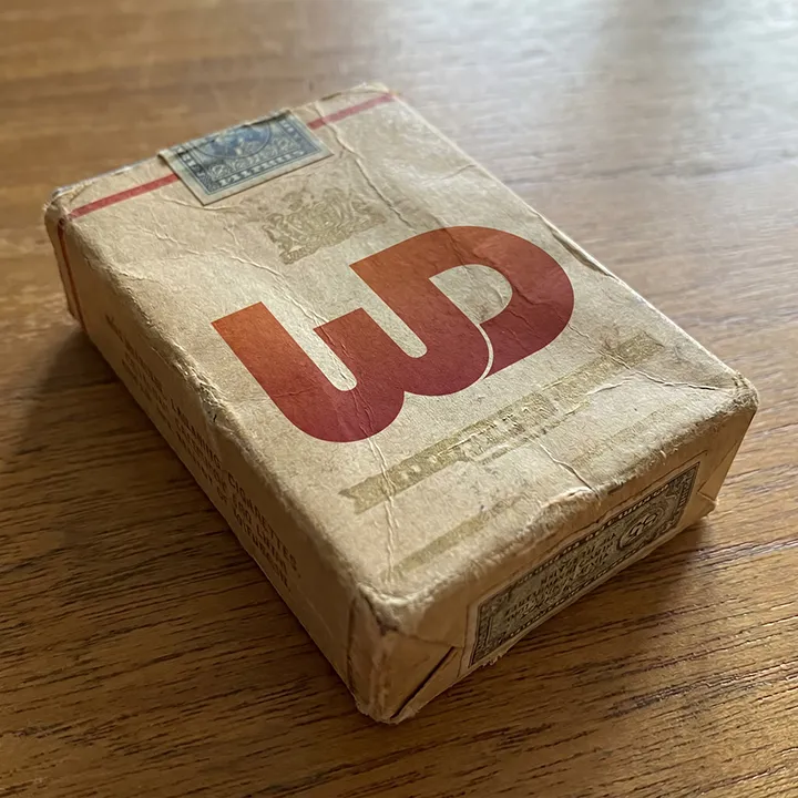 Vintage, weathered paper pack on a wooden surface featuring a prominent red Womp Designs logo.
